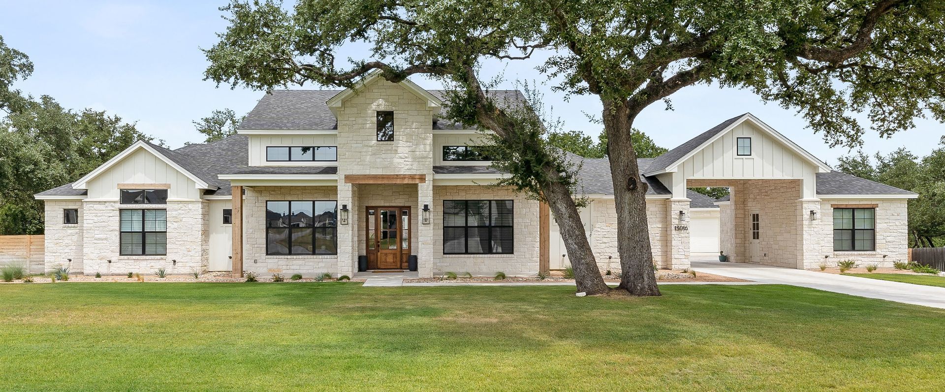 A two-story white stone farmhouse with a large tree in the yard and an attached porte-cochère.
