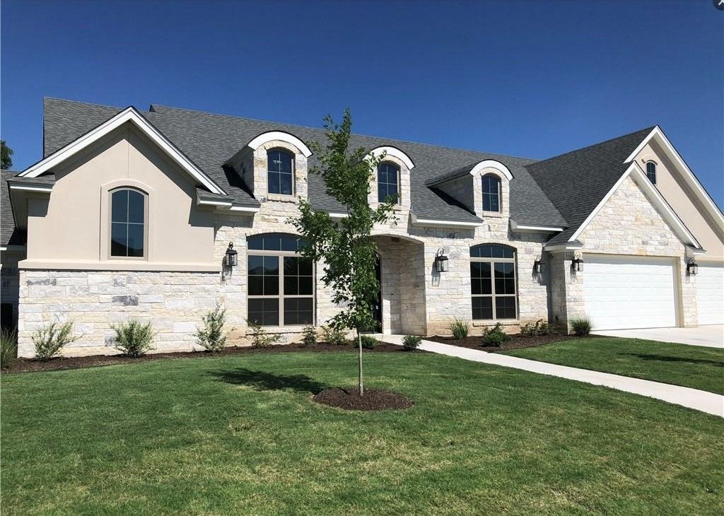 House exterior, stone and stucco facade, three dormers, green lawn, blue sky.