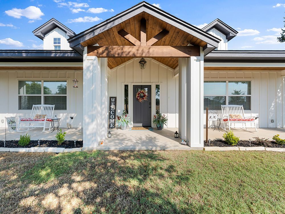 White farmhouse exterior with a porch, front door, and wooden beams.
