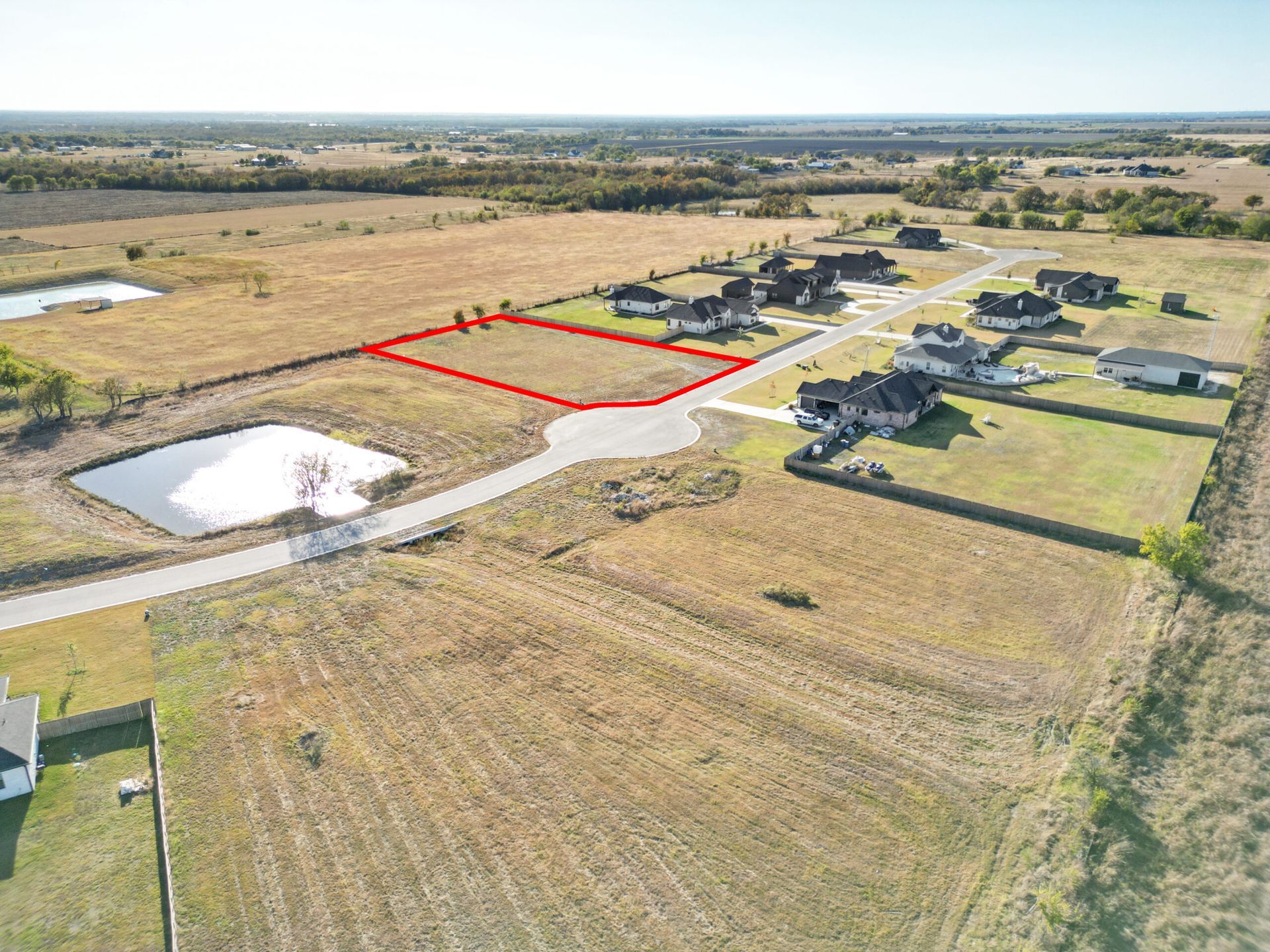 Aerial view of a vacant lot outlined in red, next to a pond and residential homes.