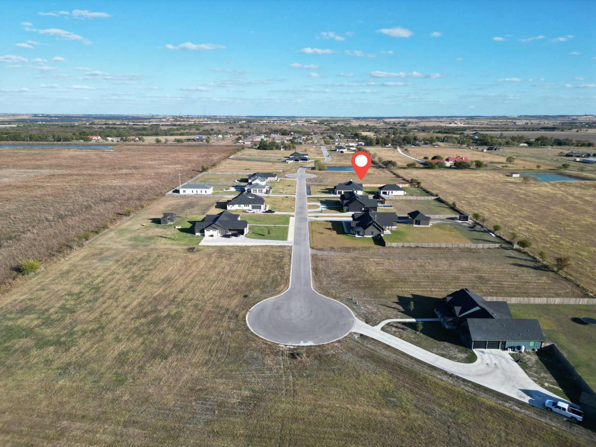 Aerial view of a suburban neighborhood with houses, a cul-de-sac, and surrounding farmland under a clear sky.