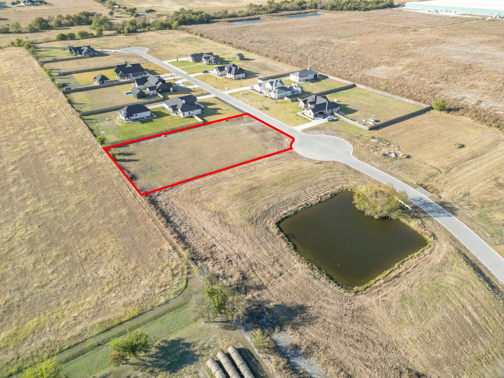Aerial view of a vacant lot outlined in red, located in a residential area with a pond.