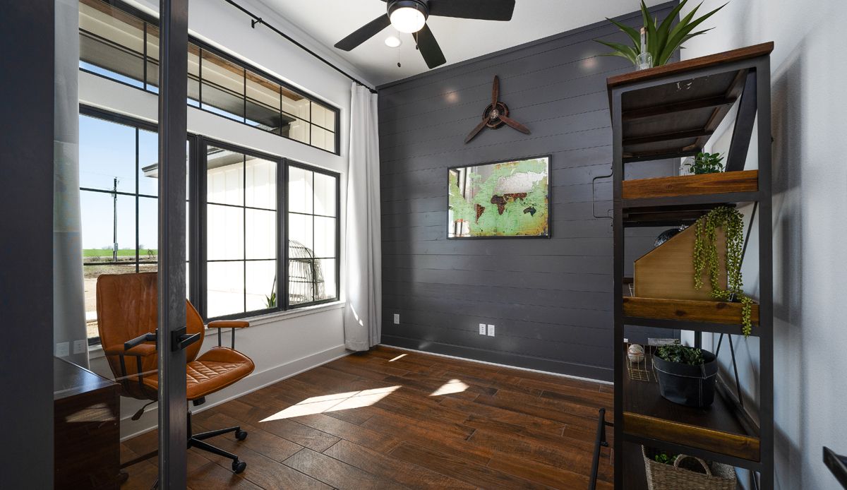 Home office with leather chair, dark wall, bookshelf, window, and world map.