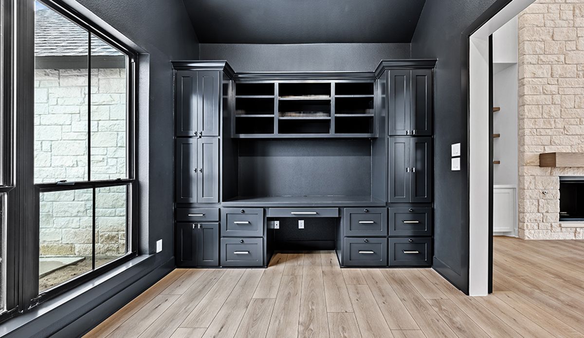 Dark gray home office with desk, cabinets, and window.