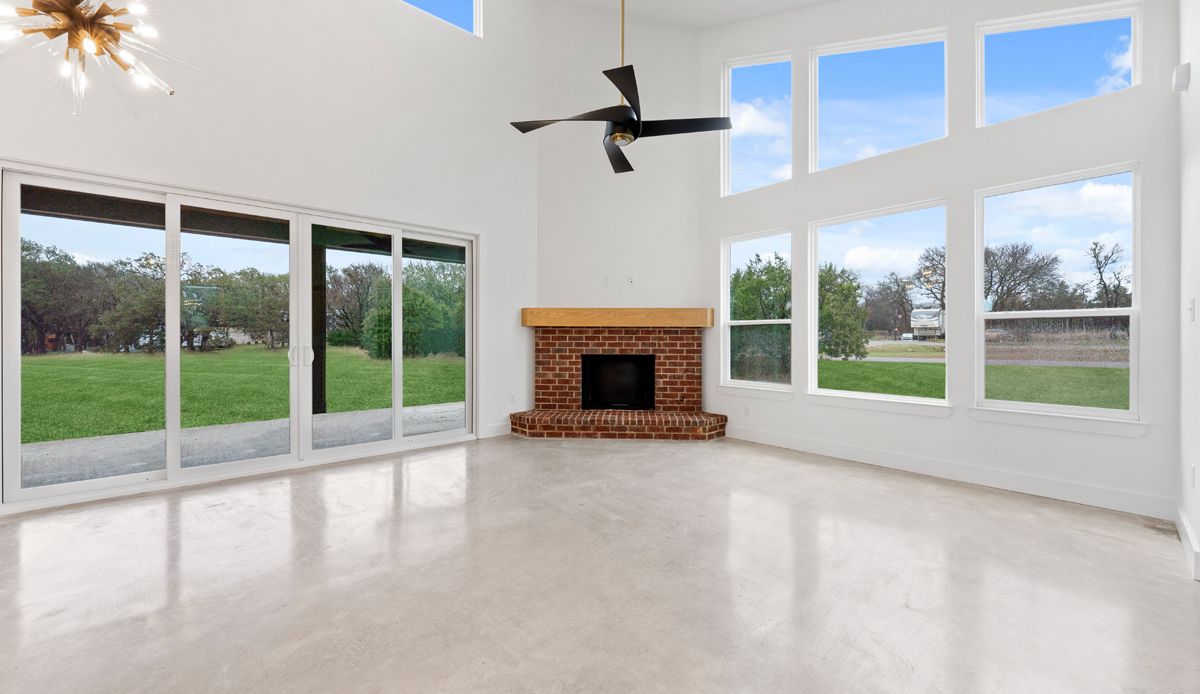 Bright, empty living room with large windows overlooking a grassy yard. A fireplace and ceiling fan are also visible.