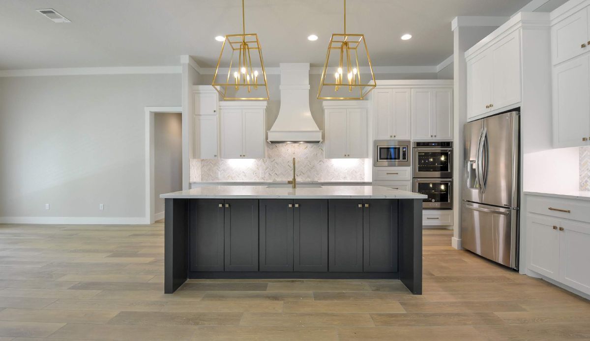 Modern kitchen with white and dark gray cabinets, island, stainless steel appliances, and gold light fixtures.