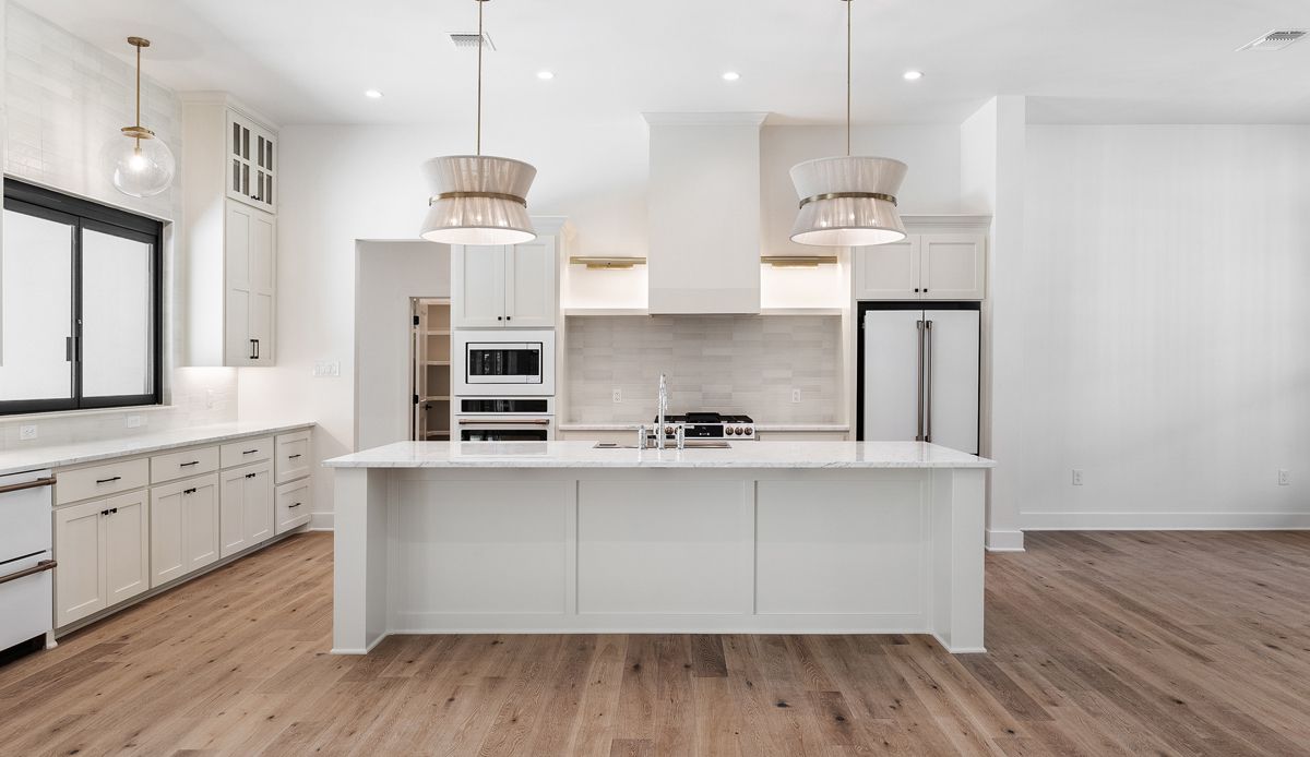 Modern white kitchen with island, wooden floors, pendant lights, and stainless steel appliances.