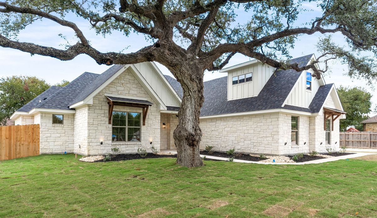 House with light stone siding, black roof, and large tree in the front yard.