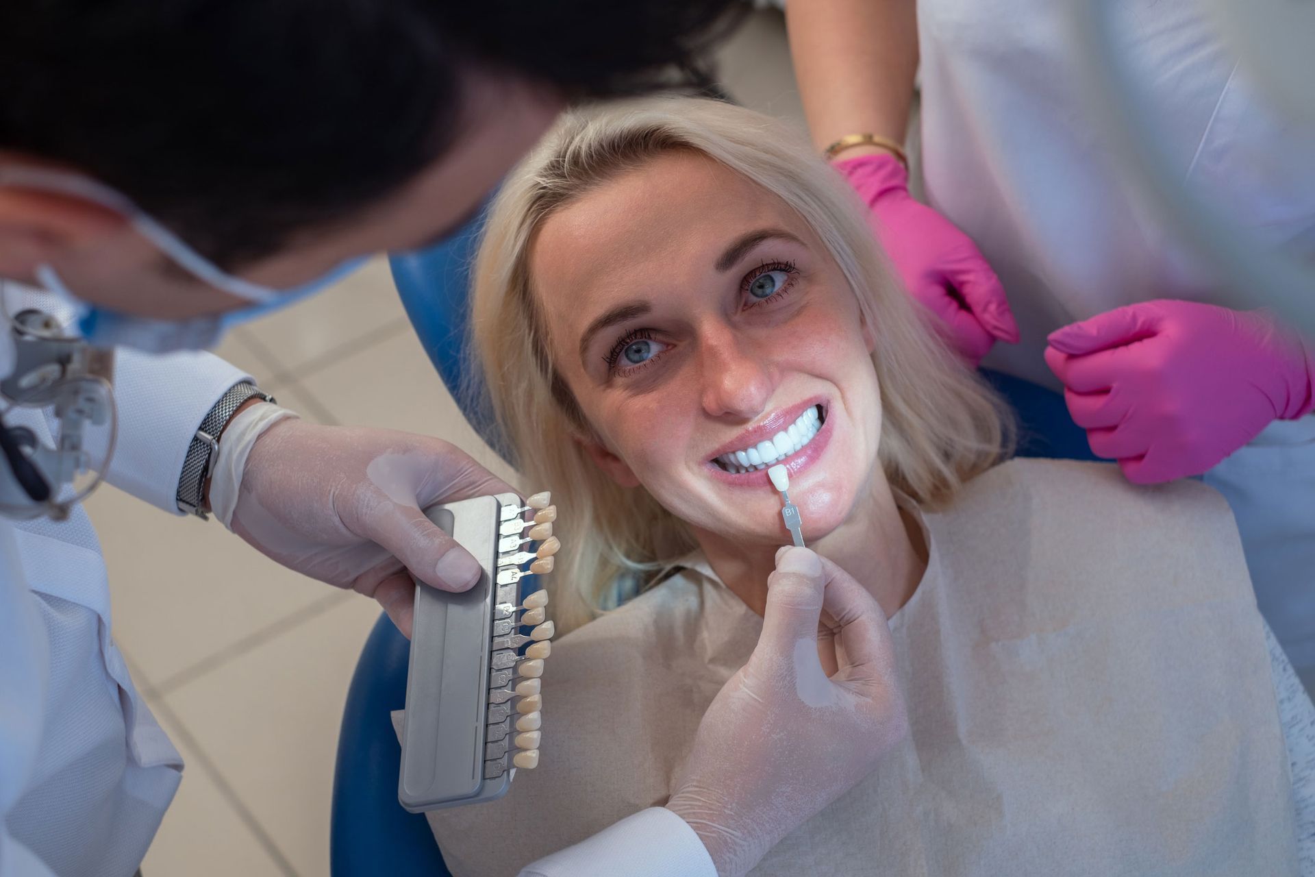 A woman is sitting in a dental chair while a dentist examines her teeth.
