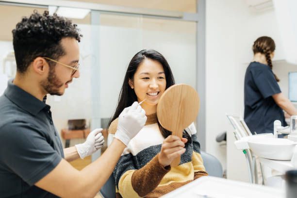 A woman is looking at her teeth in a mirror at the dentist.