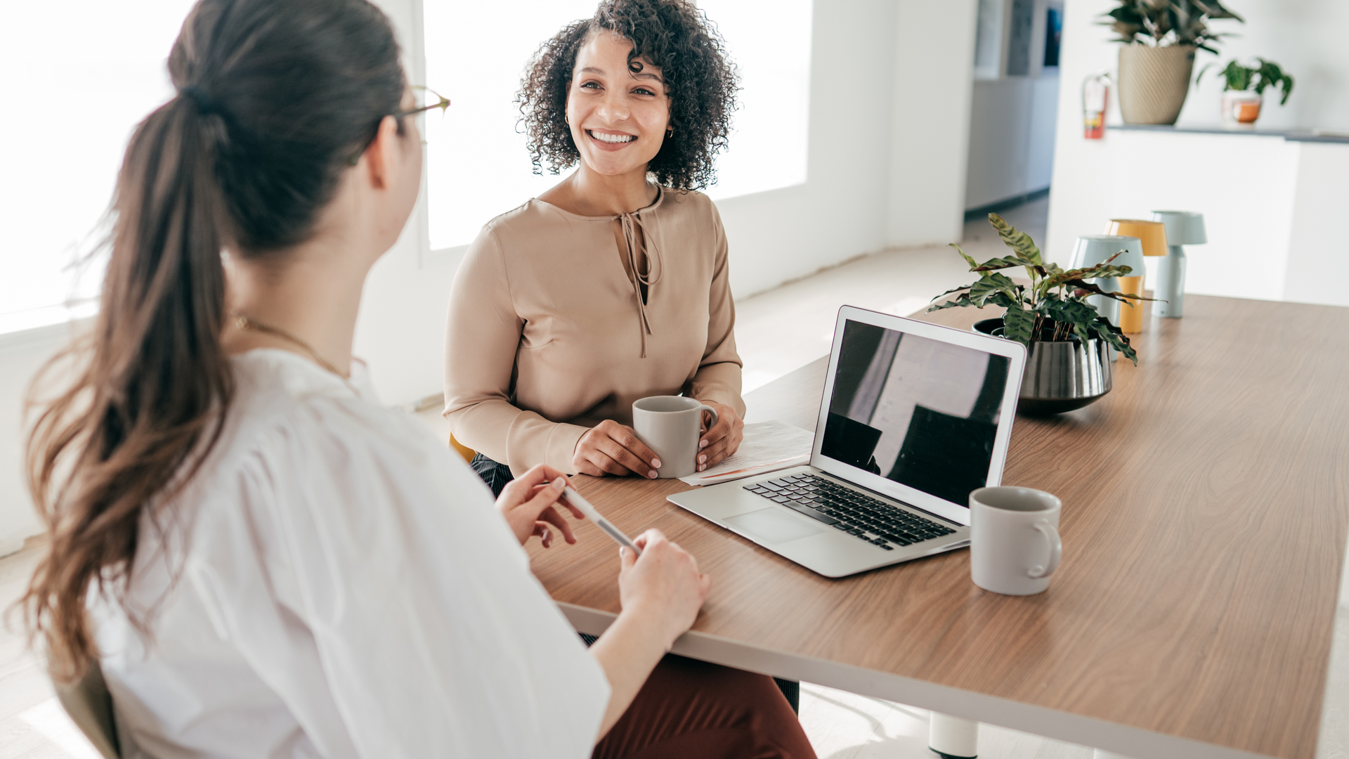 Two women are sitting at a table with a laptop.