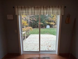 Sliding glass door with a view of a deck and fall foliage, framed by a striped valance.