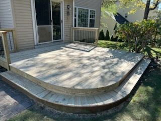 Wooden deck with curved steps leading to a yard, next to a house with a sliding glass door.