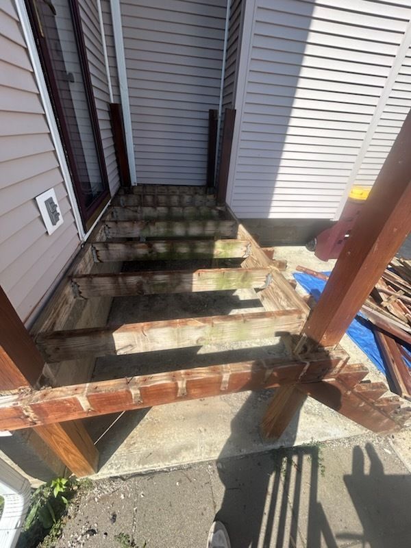 Damaged wooden exterior stairs leading to a building's entrance. The stairs are missing treads and in disrepair.