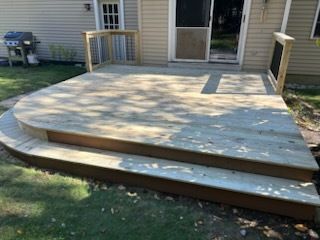 Wooden deck with curved edge and steps, adjacent to a house with a door.