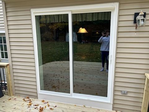 Sliding glass door on a deck, with a person reflected in the glass, set against a beige house.