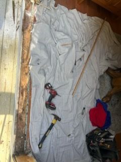 White cloth covering debris near a wooden wall, with tools like a drill and hammer visible.