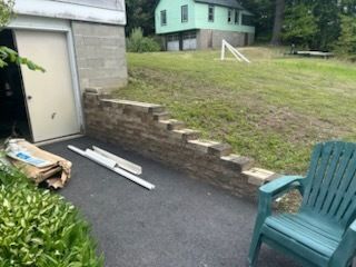 Brick wall stairs beside garage door and green plastic chair in yard.