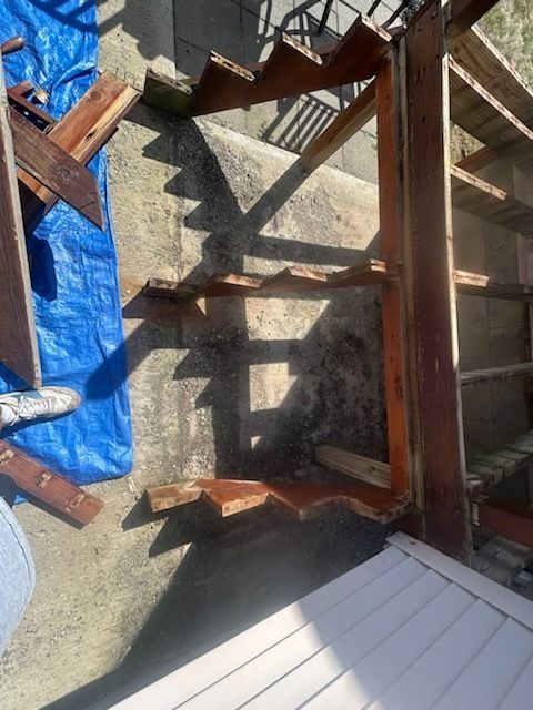 Outdoor wooden staircase with weathered concrete steps and side support. Blue tarp and debris on the left.