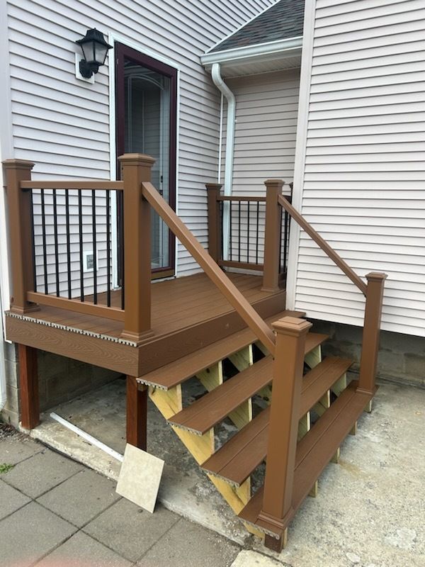 Brown deck and stairs attached to a house with beige siding. Black railing and trim.