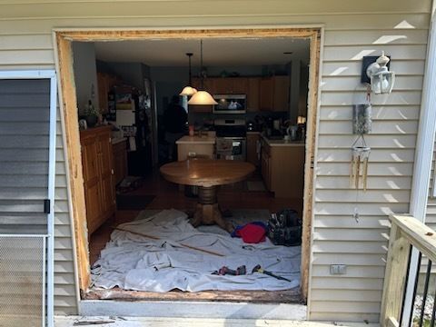 Opening in a house's exterior wall. Reveals a kitchen interior, work debris on floor, and part of a deck outside.