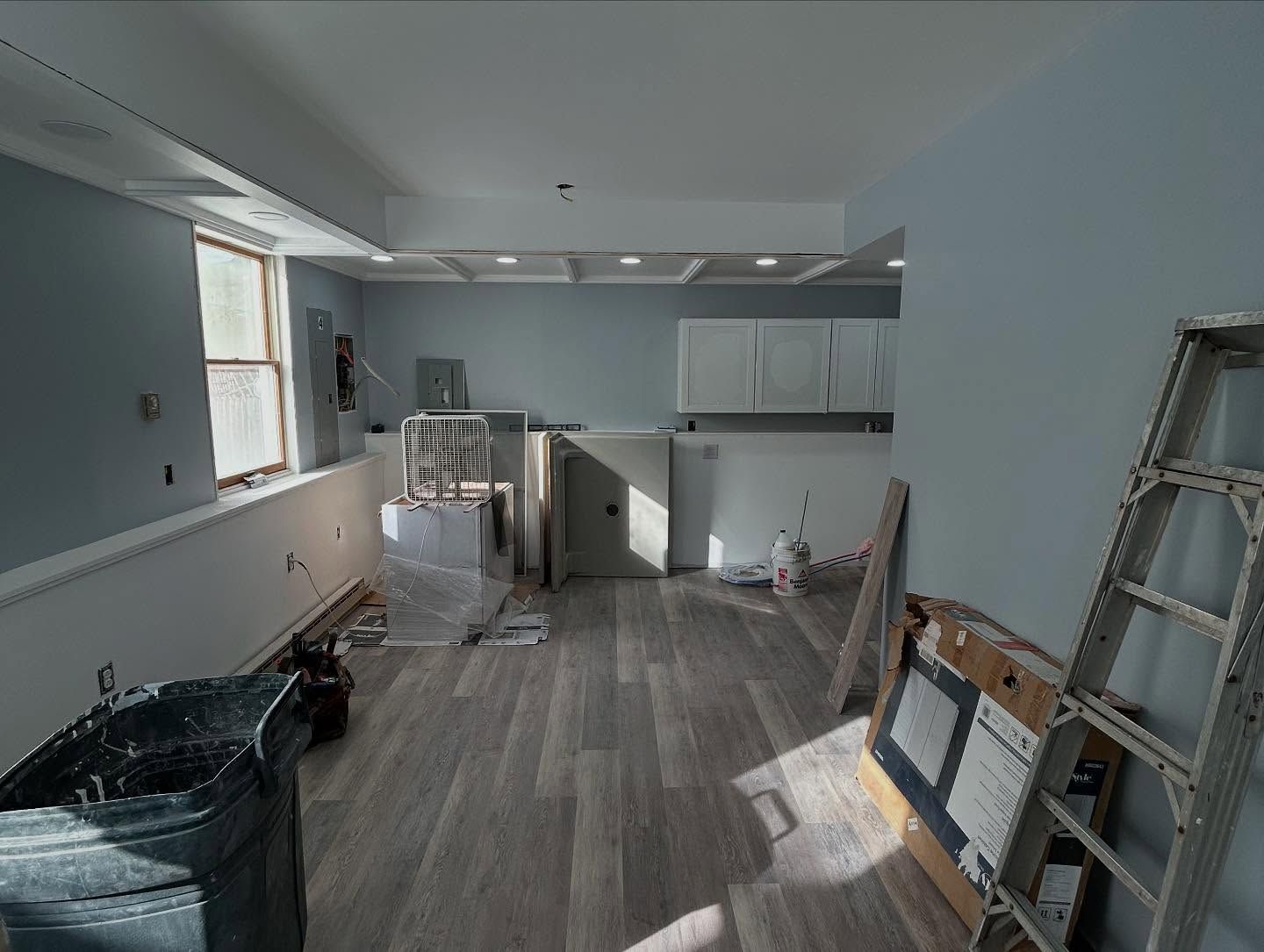 Interior of a room under construction with pale blue walls, wooden floors, and a ladder on the right.