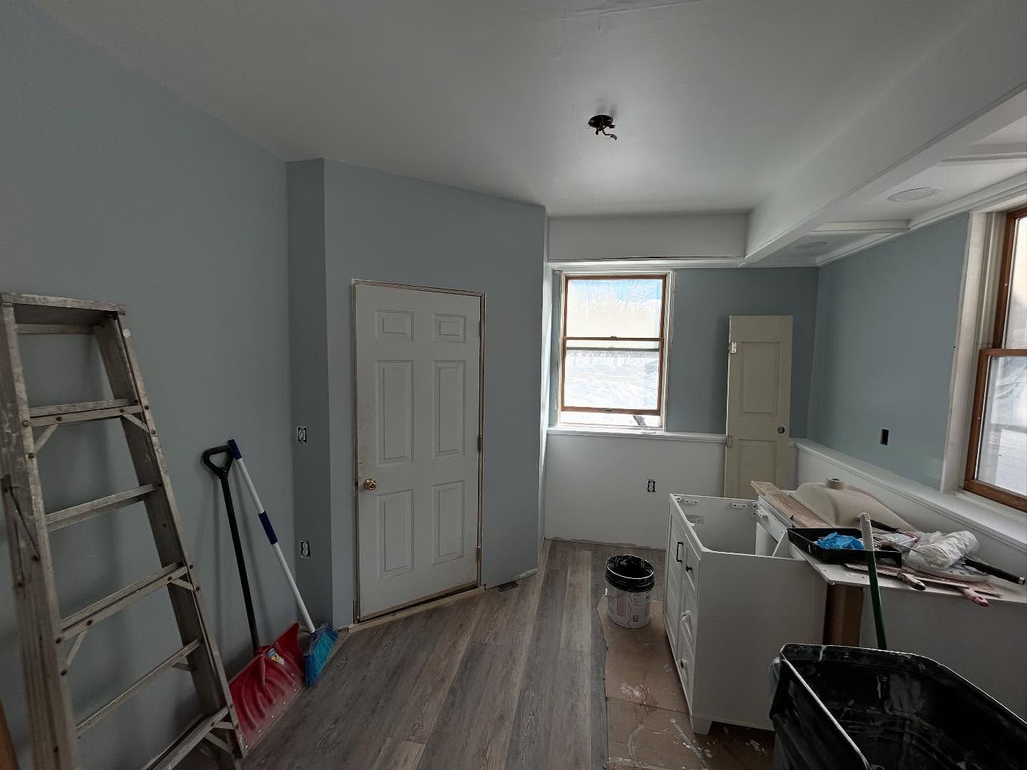 Room interior with blue-painted walls and a partially finished renovation. Includes a ladder, door, and window.
