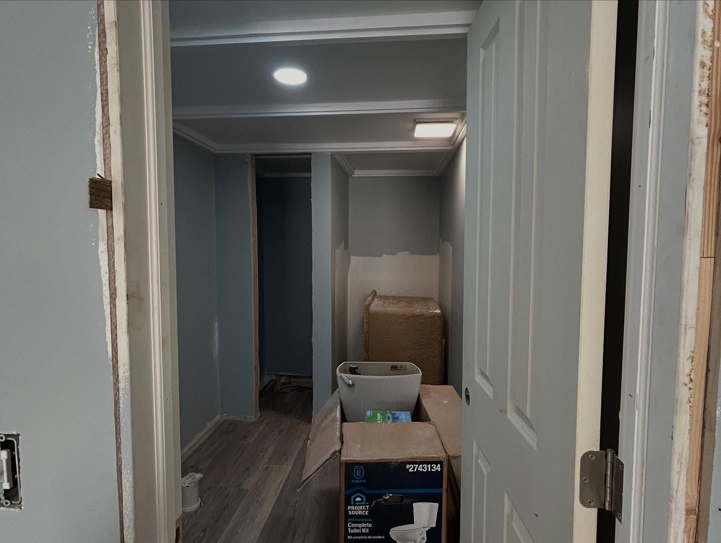 Interior hallway under renovation, with doorways, new flooring, and unfinished walls painted light blue.