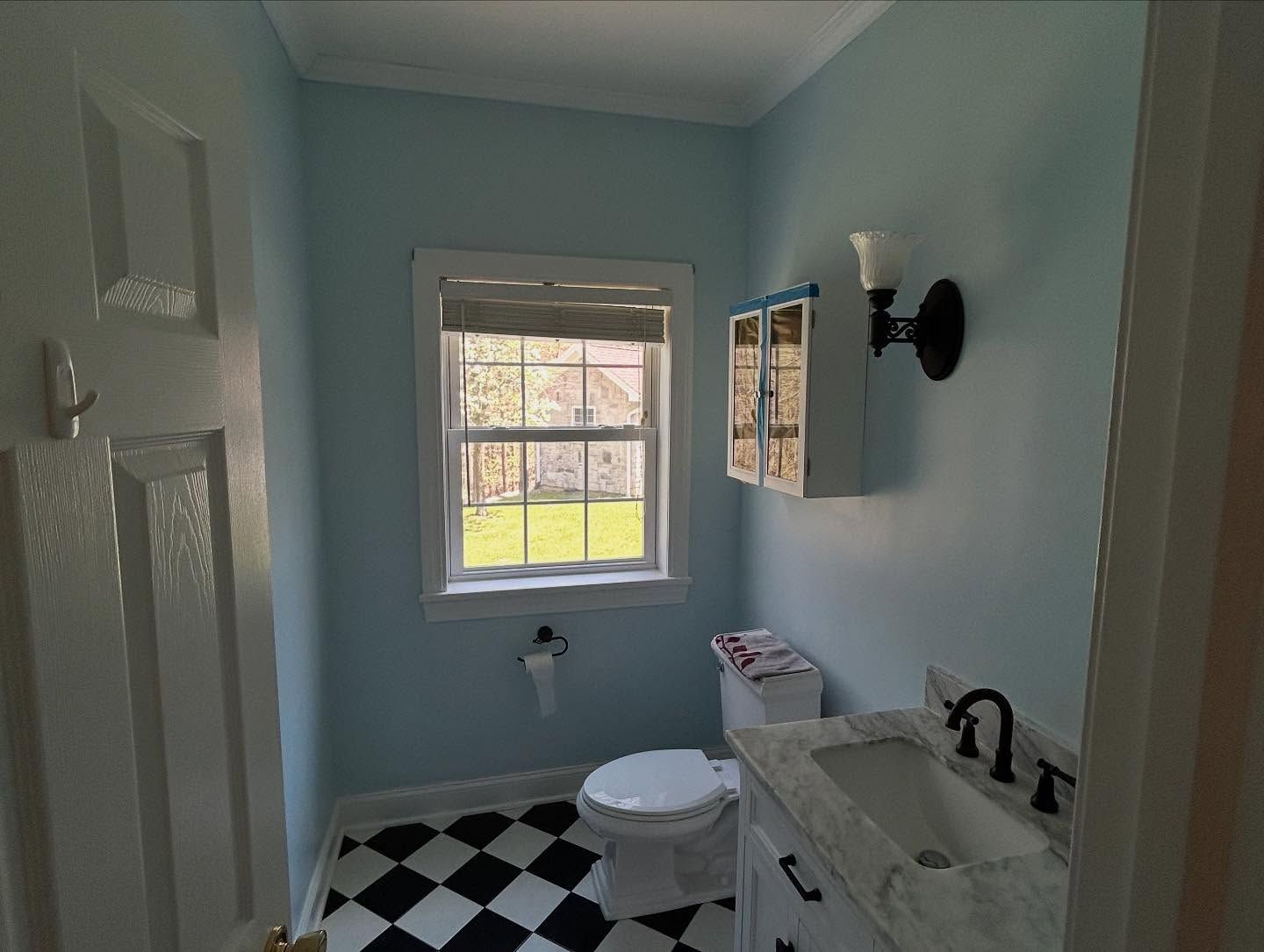 Powder room with blue walls, black and white checkered floor, and a window.