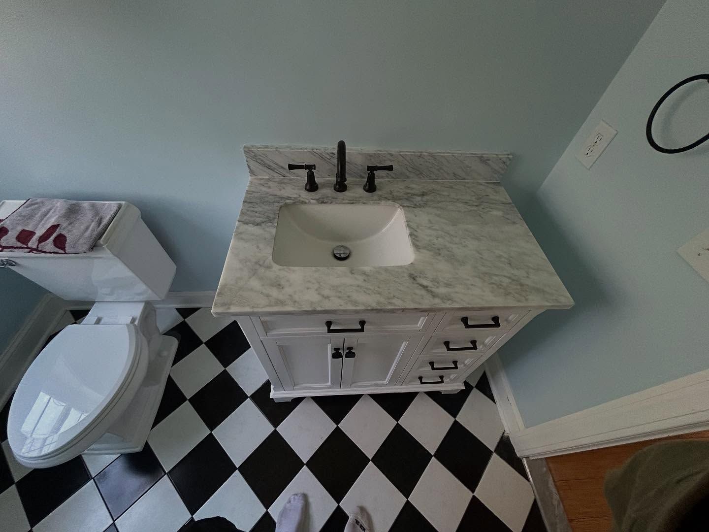 Bathroom with a white vanity, marble countertop, black faucet, and black and white checkered floor.