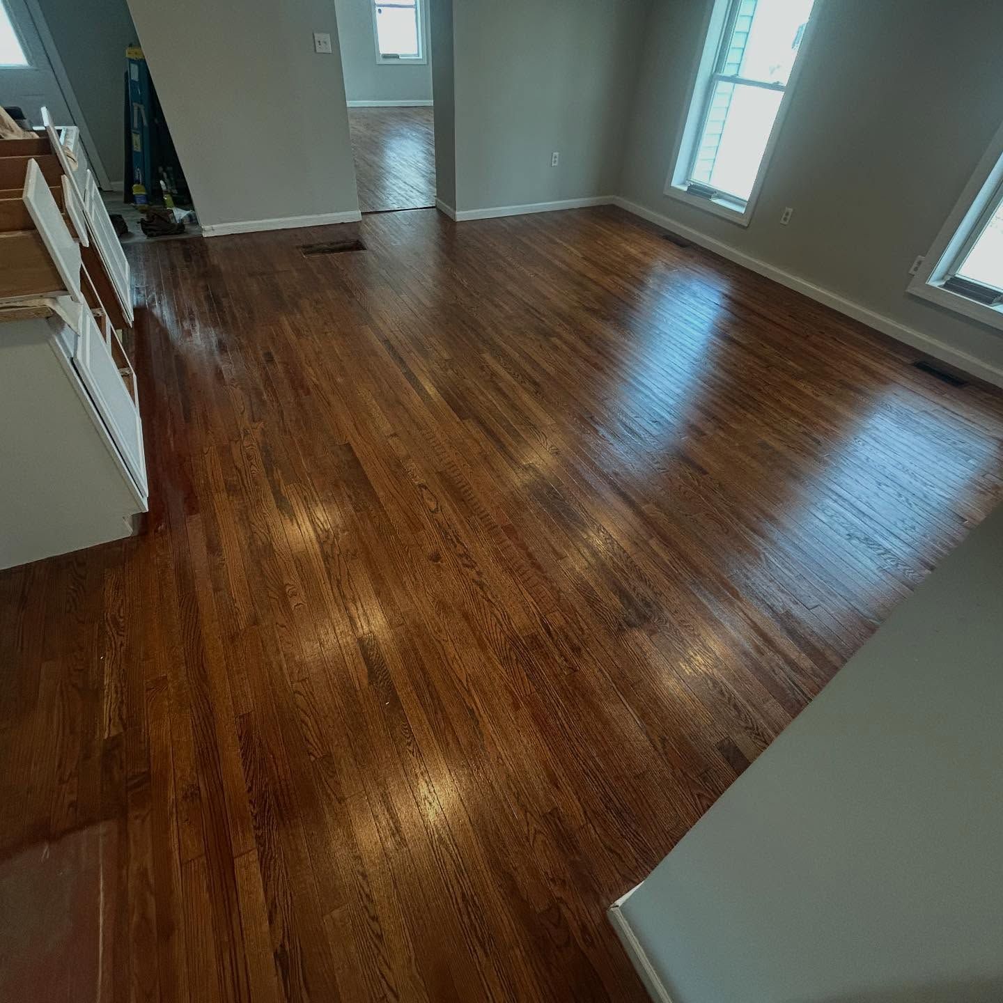 Hardwood floor reflecting light in a room with windows and a staircase.
