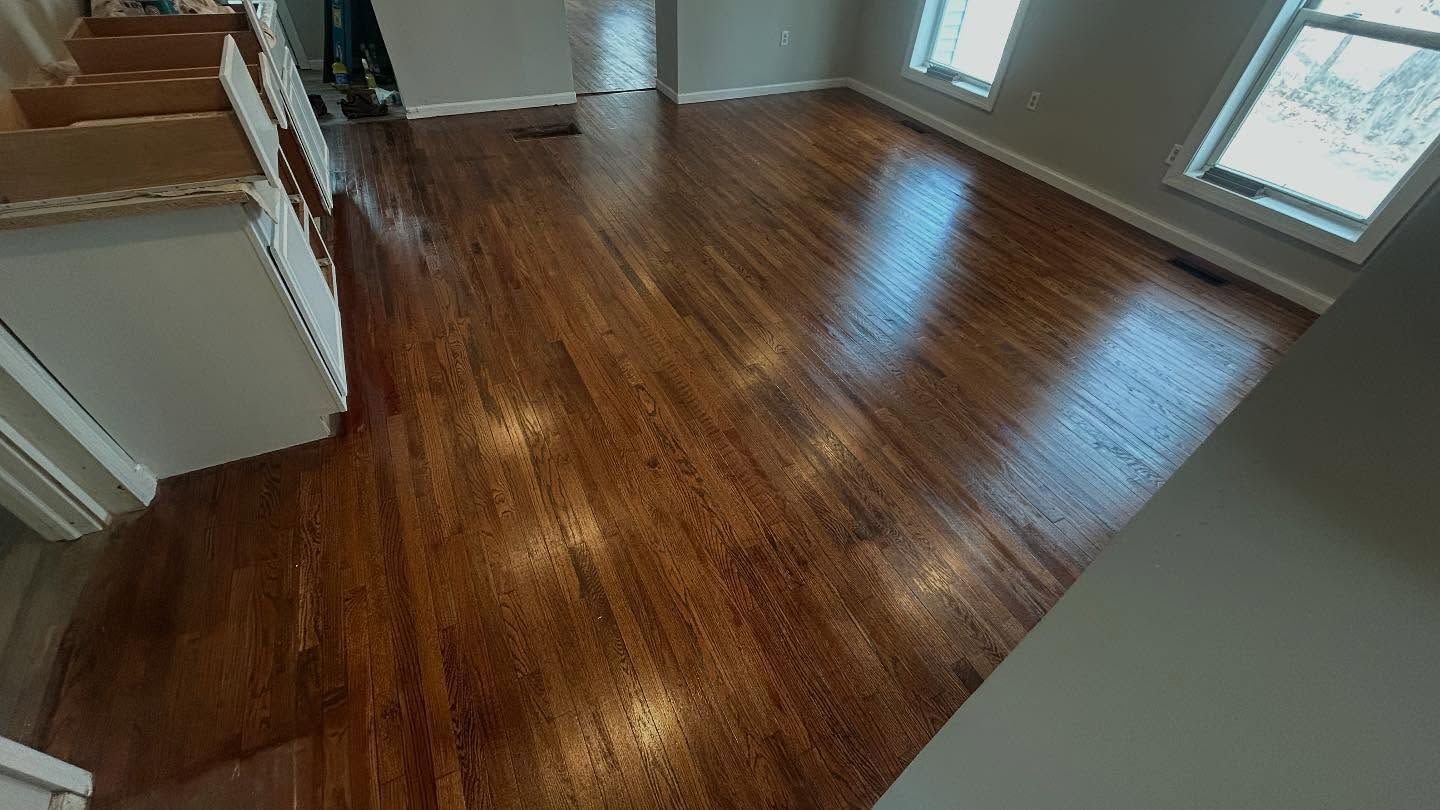 Shiny, dark wood floors in a room with white walls and two windows, reflecting light.