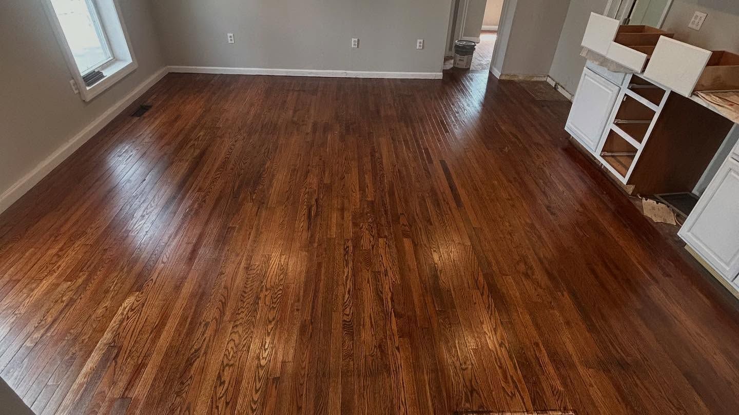 Newly finished hardwood floor in a room with white cabinets and a window.