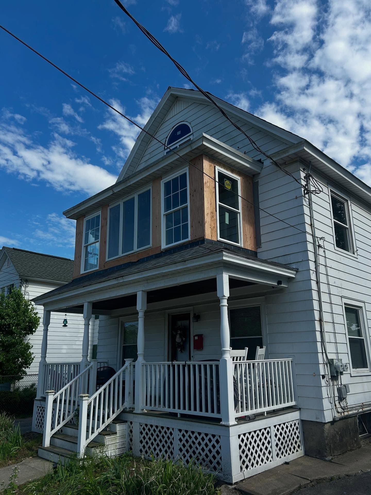 Two-story house with porch, white siding, and windows. Construction work visible on the second floor, blue sky.