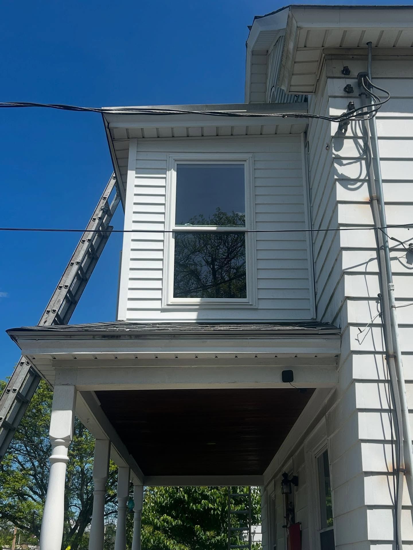 White house exterior with window and porch, ladder against side, blue sky.