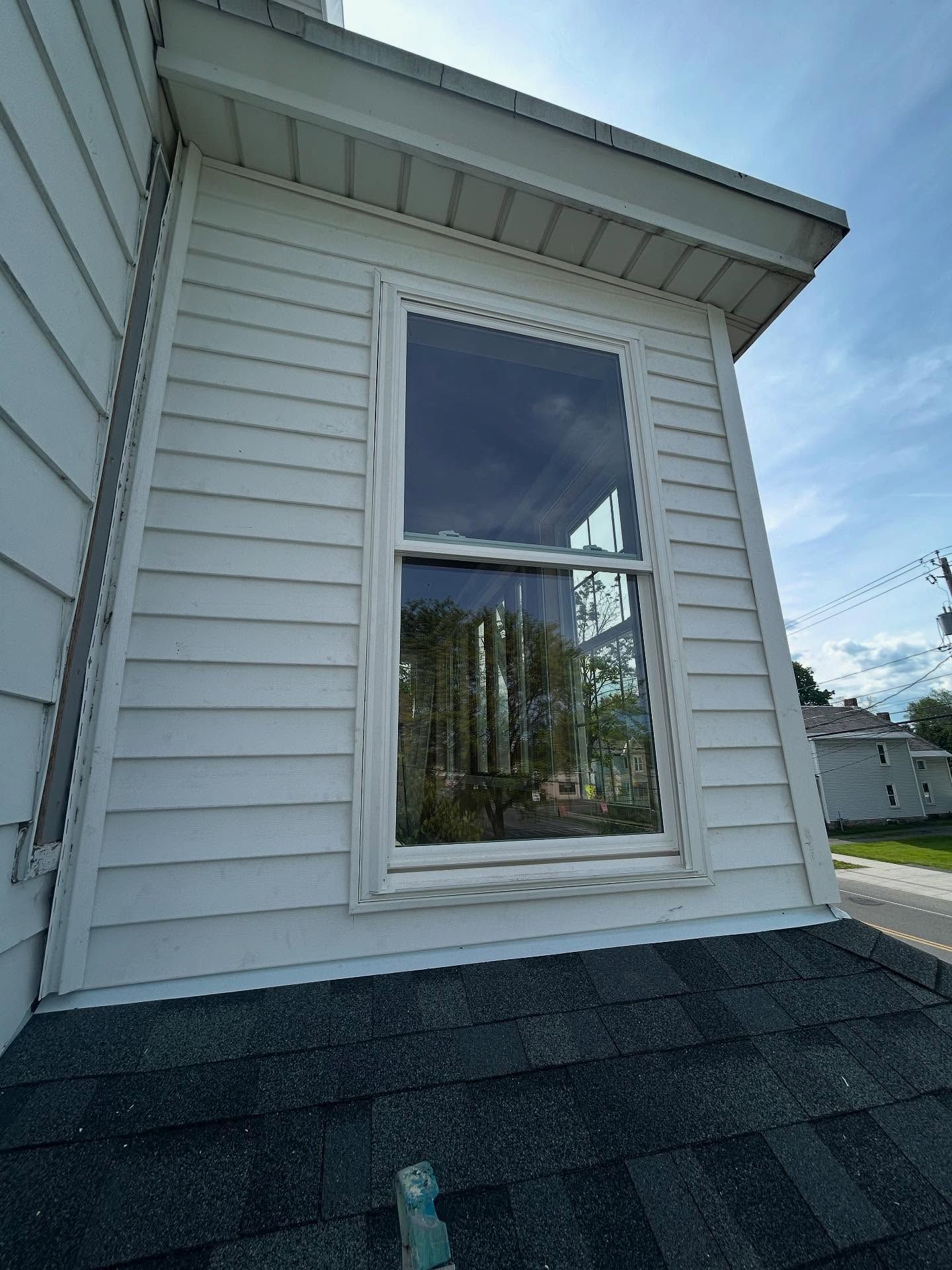 White siding with a window, part of a house roof visible. Reflection in window.