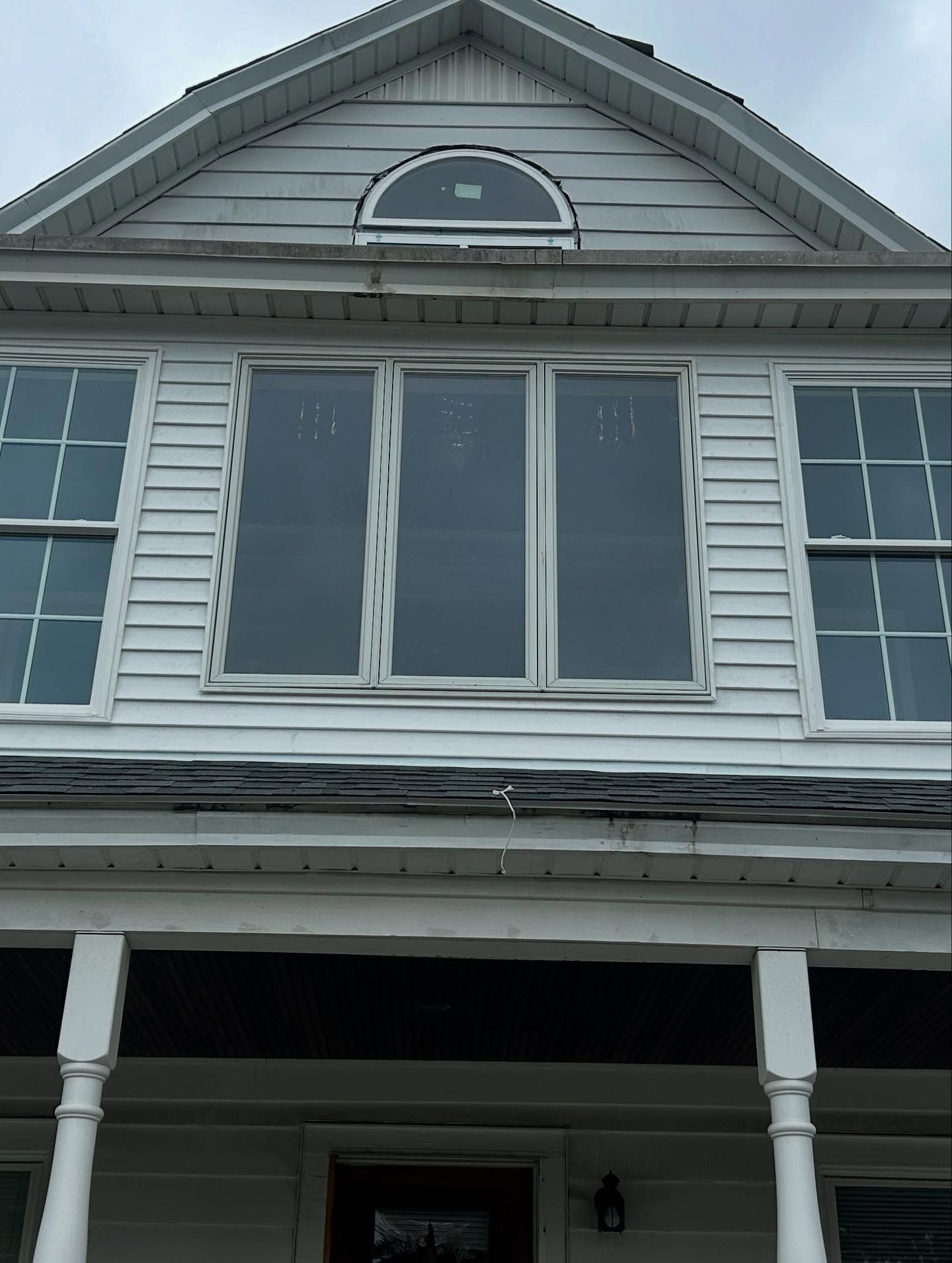 White two-story house with front porch and large windows under a cloudy sky.
