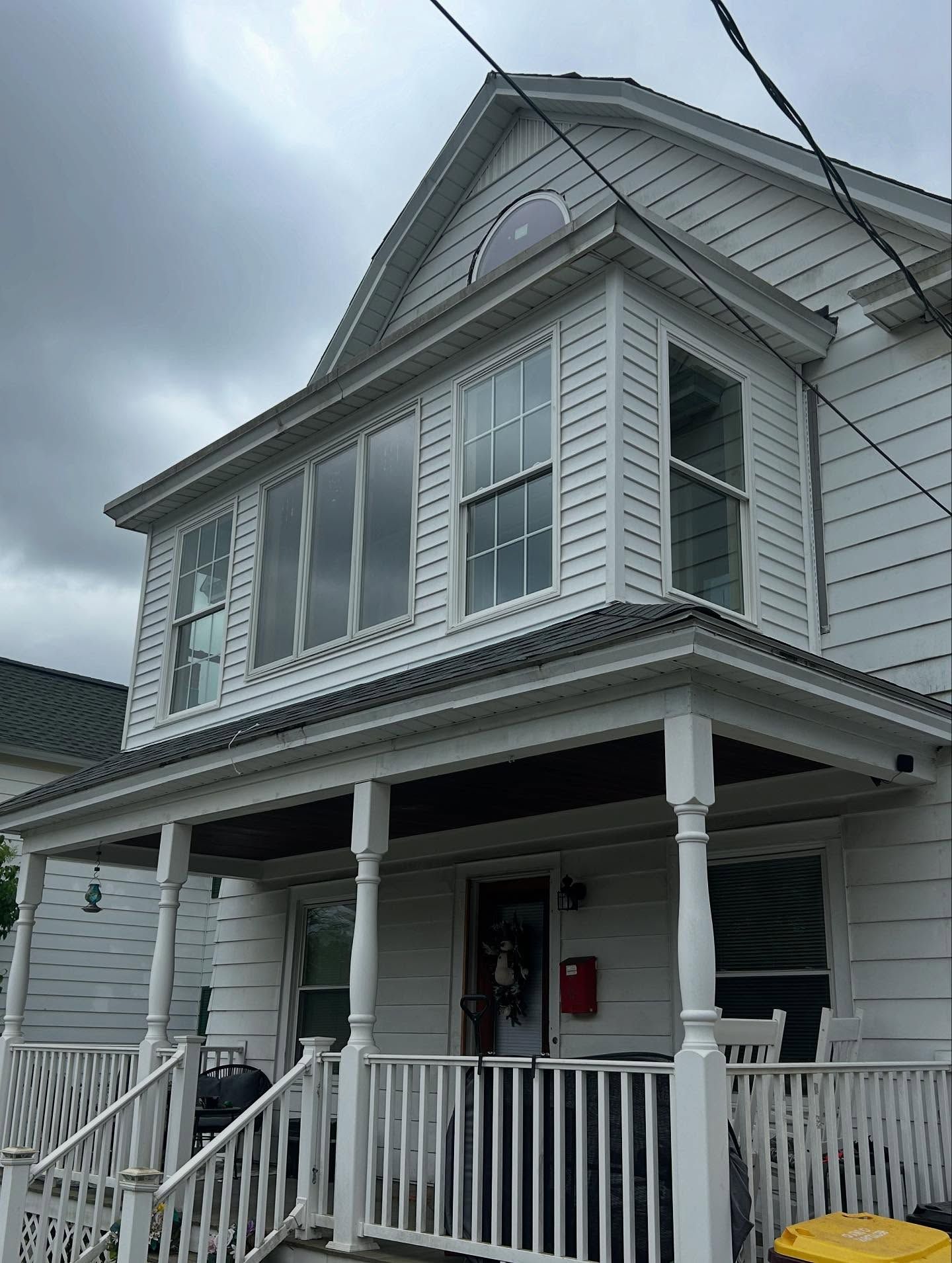 White two-story house with porch, windows, and gable roof; cloudy sky in the background.