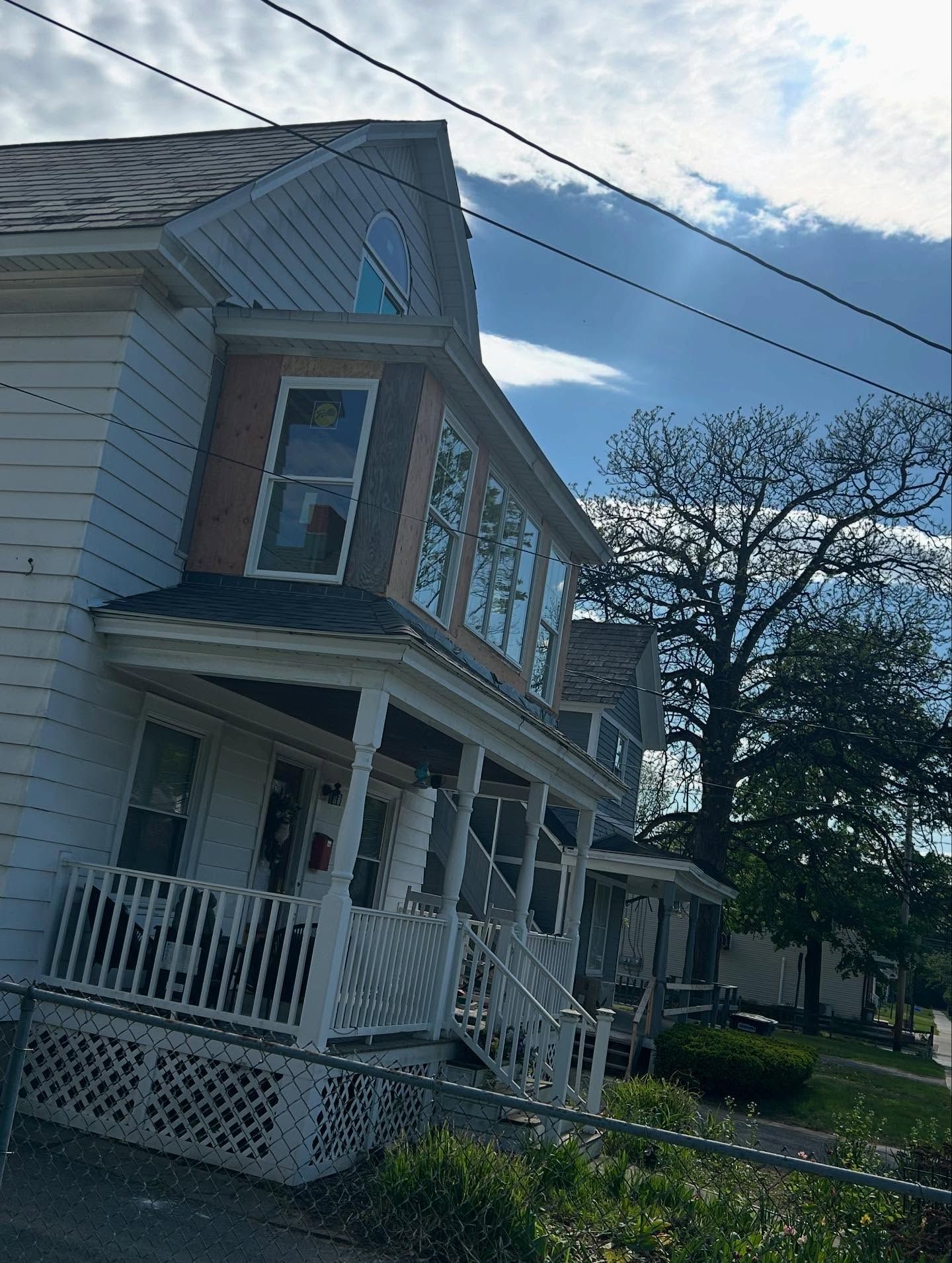 Two-story house with porch, white siding, and several windows on a sunny day.