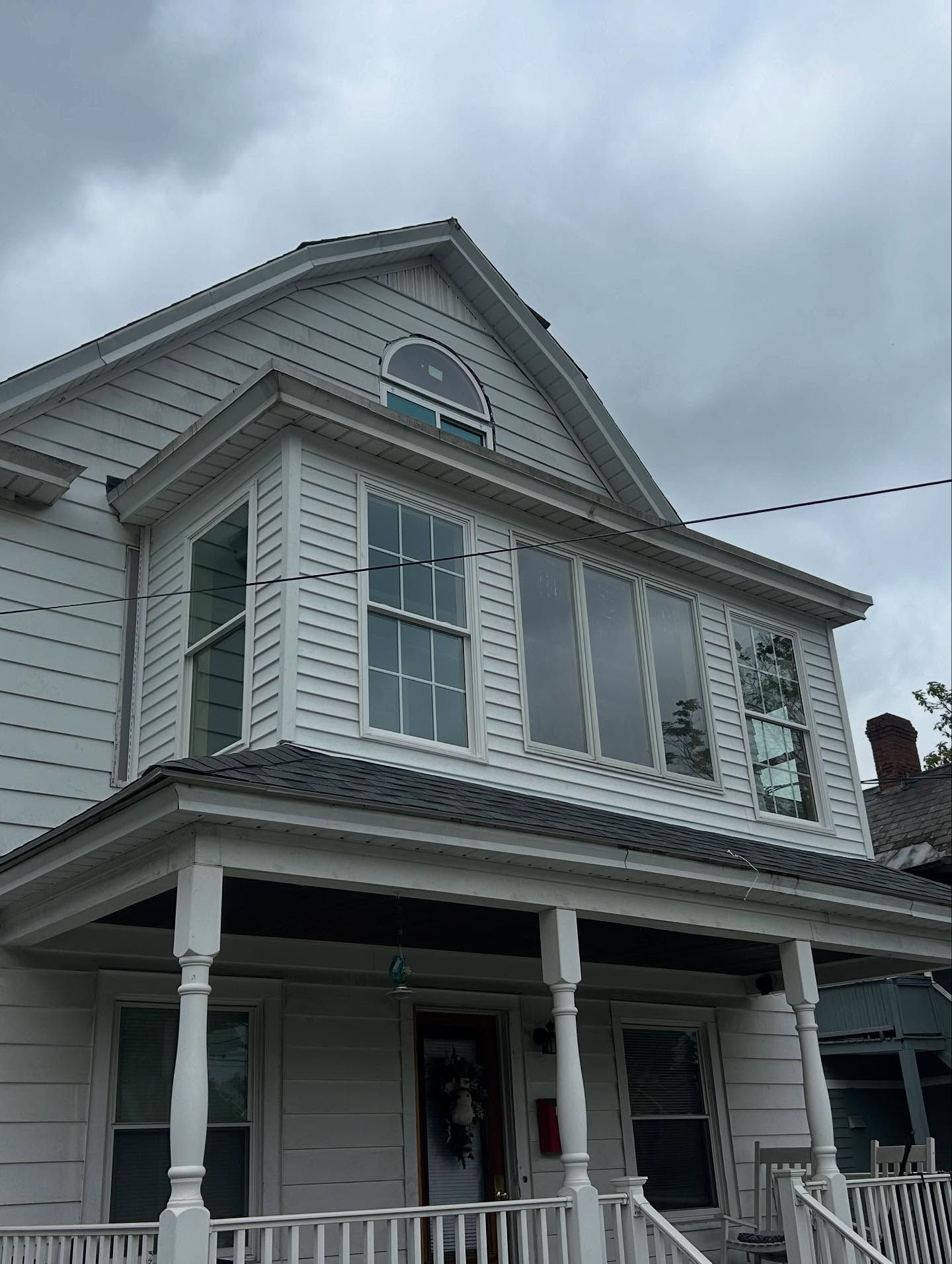 White house with porch and multiple windows under a cloudy sky.