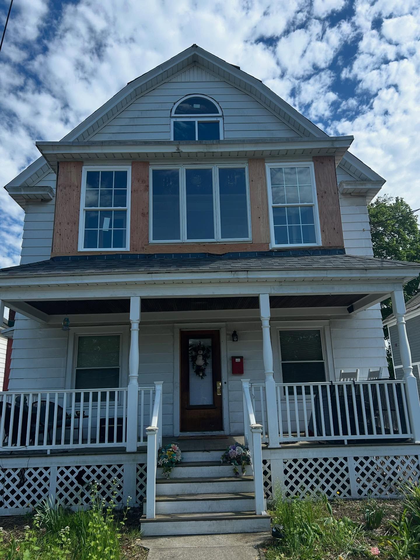 Two-story white house with porch and ornate trim, under a partly cloudy blue sky.