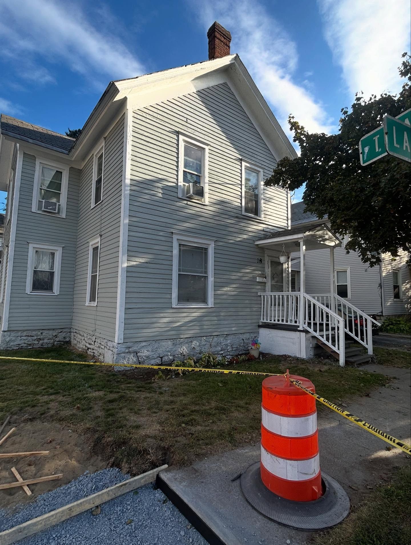 Two-story house with gray siding, white trim, and a small porch. A construction zone is in front.