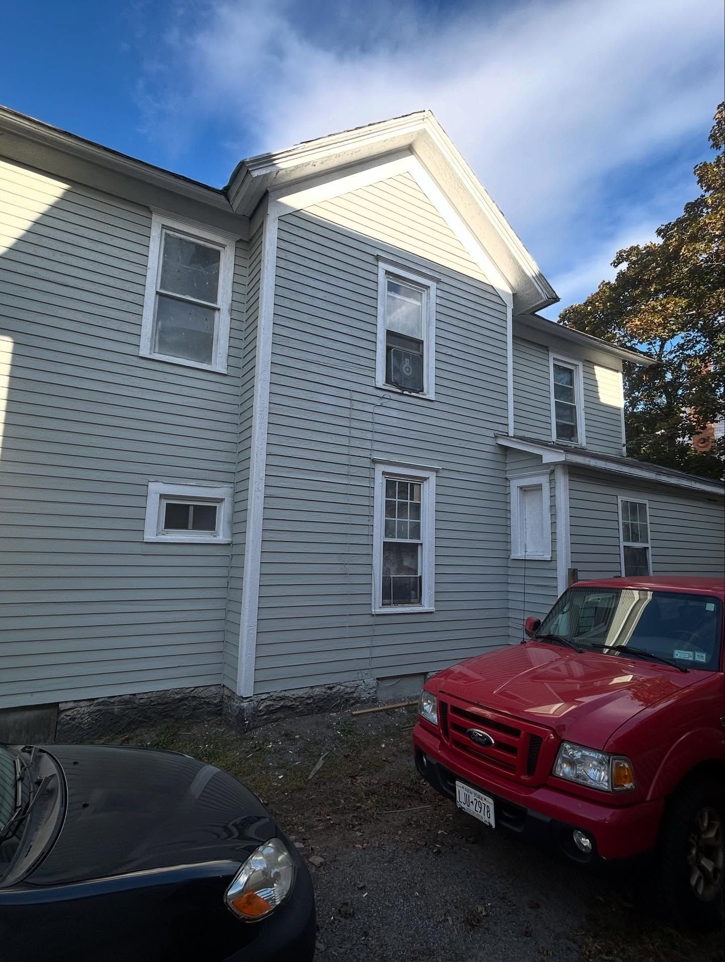 Two-story light gray house with white trim; red truck and dark car parked in front.