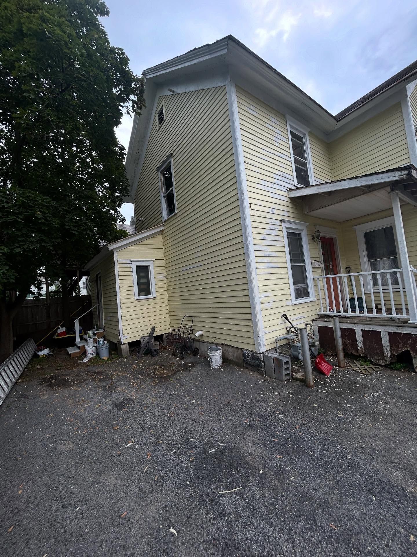 Yellow building with white trim, gray gravel parking, and overgrown yard.