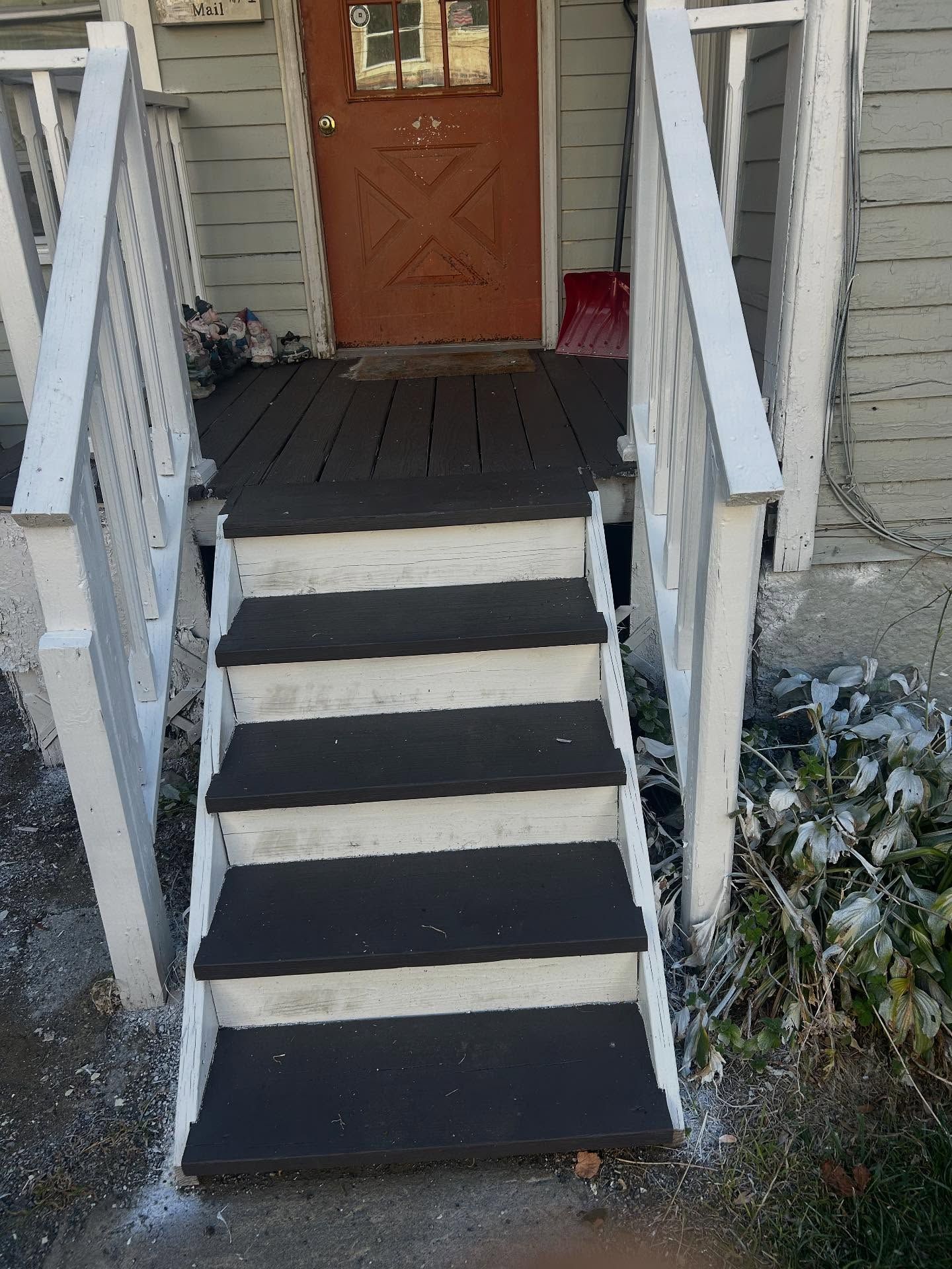 Wooden steps leading up to a porch with a brown door. White railings and dark steps.