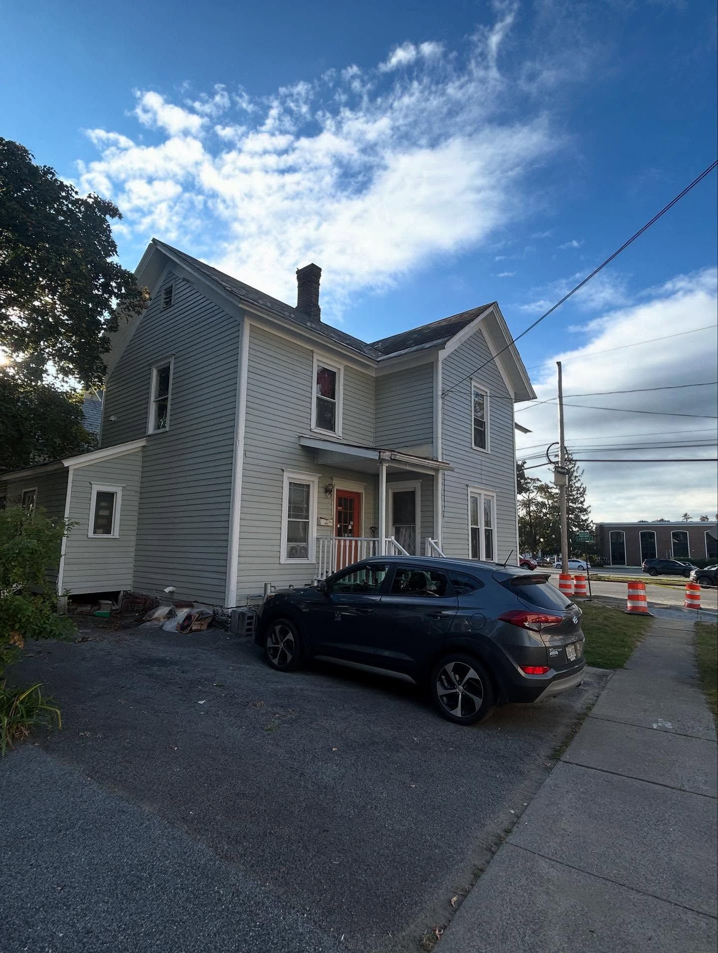 Two-story house with gray siding, parked car in front, and a blue sky.