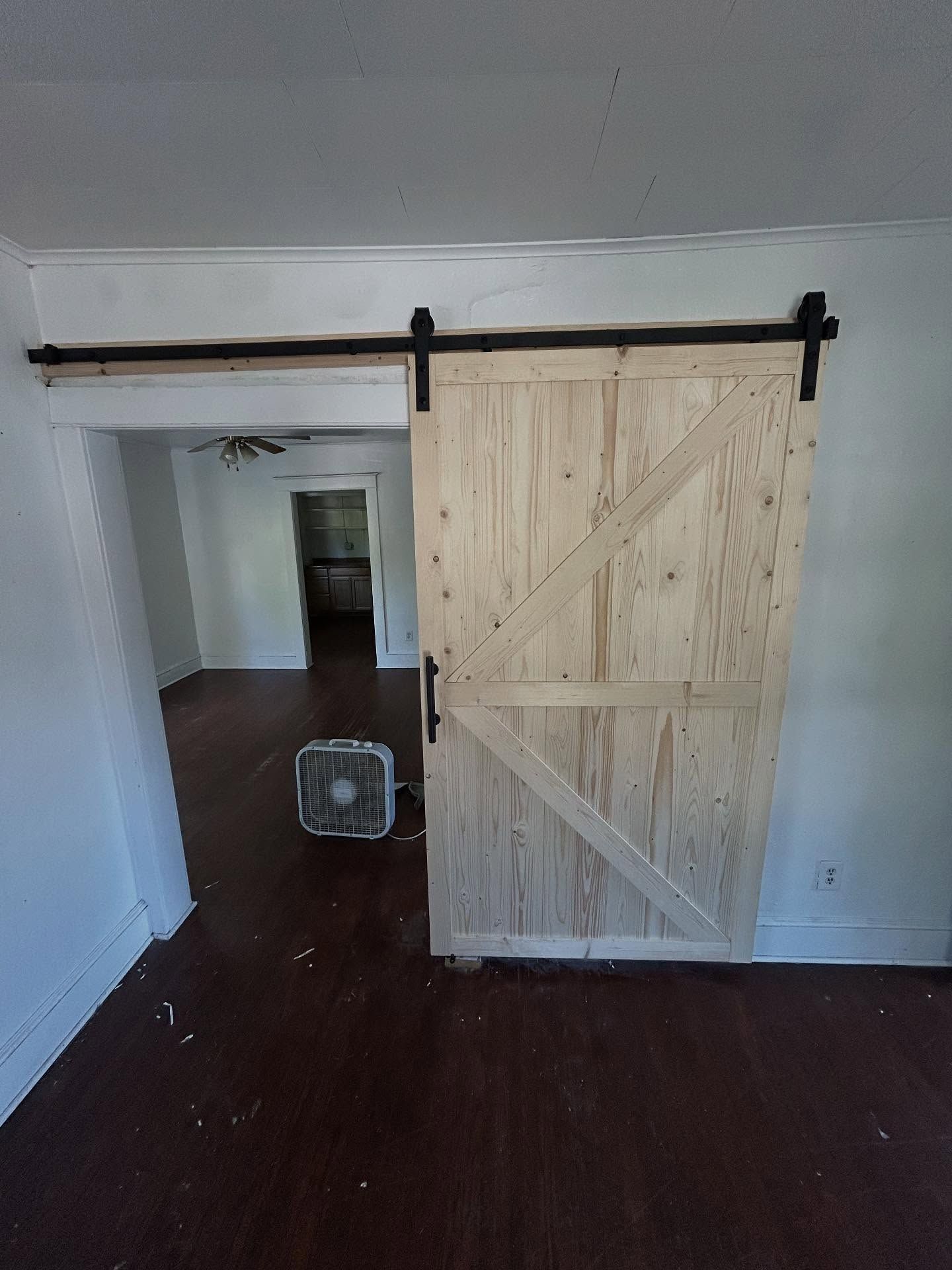 Barn door made of light wood with black hardware, covering doorway. Dark wood floor.