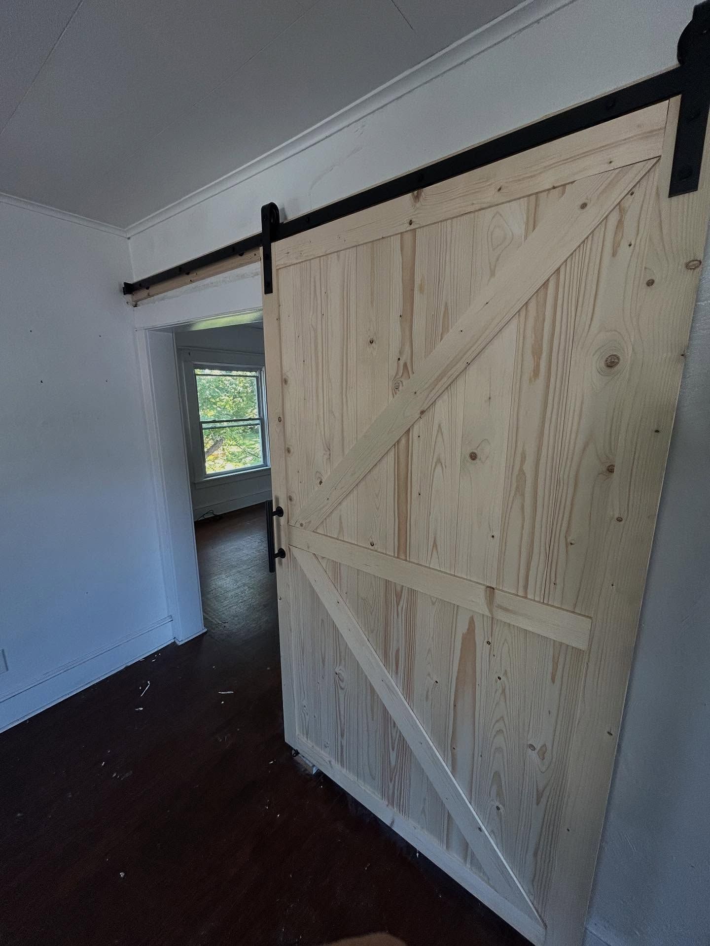 Barn door with black hardware, open, showing a room with a window and dark floor.