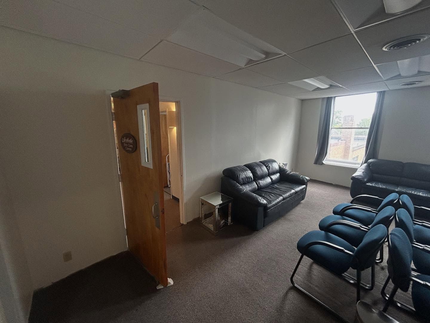 Room with couches, chairs, and a door. Carpeted floor, white walls, and a window with curtains.