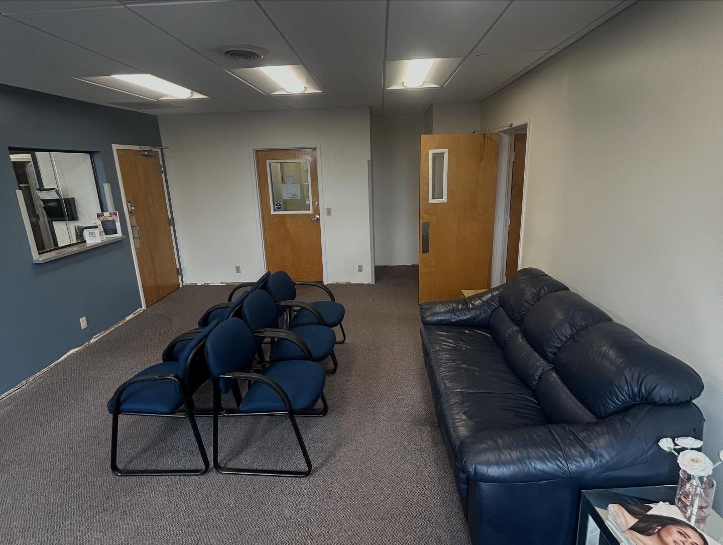 Waiting room with blue chairs, sofa, and doors.